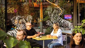 An outdoor dining area with tables and chairs, a glass window with tiger decorations, and a neon sign. - Greulich Design & Boutique Hotel (Zürich)