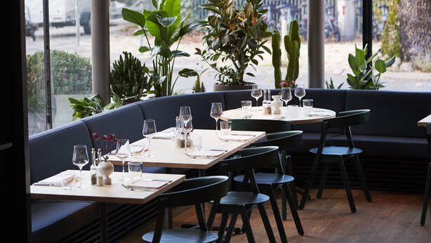 A restaurant with round tables and black chairs, large windows, and potted plants. - Greulich Design & Boutique Hotel (Zürich)