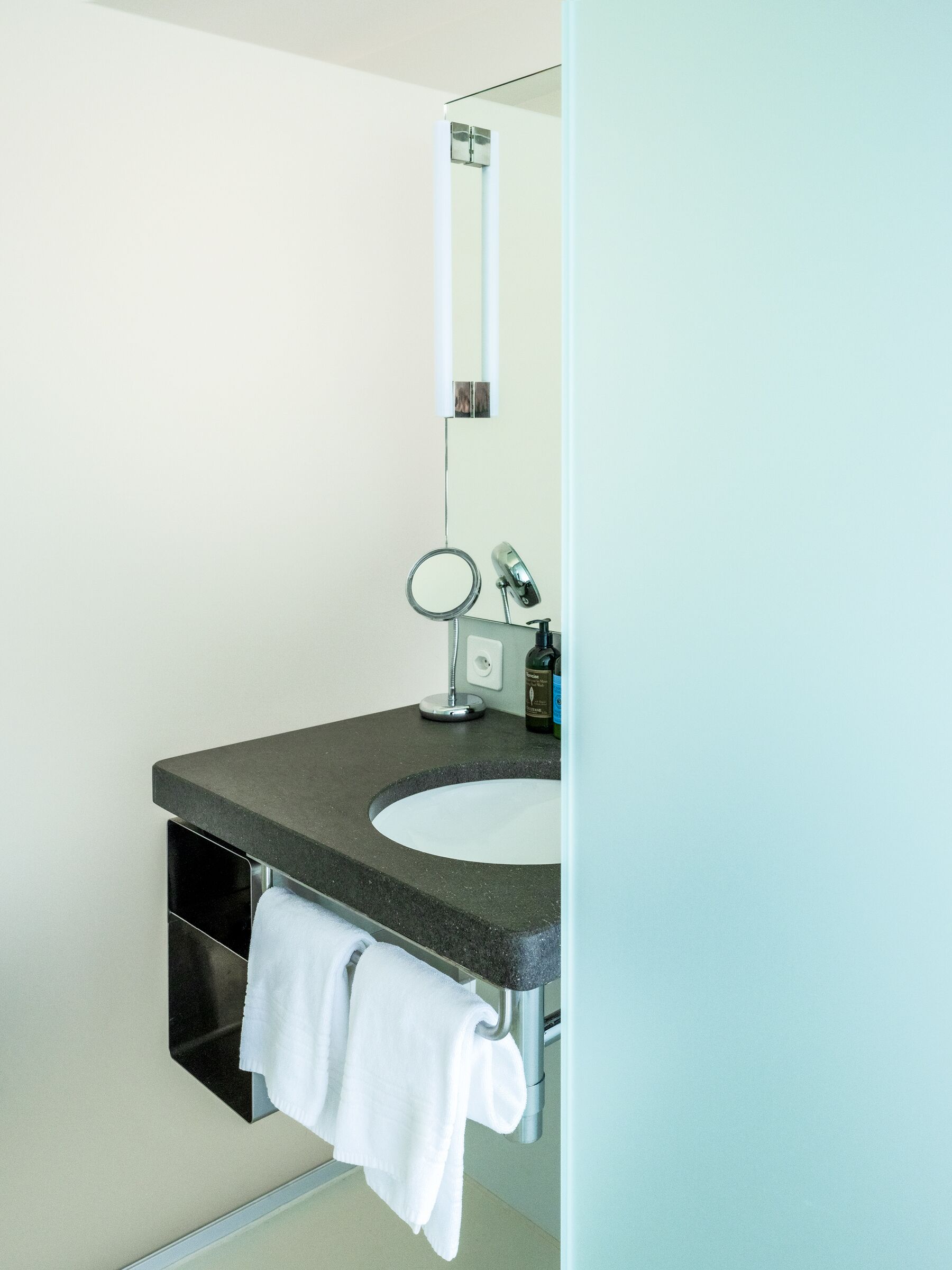 A modern bathroom with a dark granite sink, a round mirror, and a towel hanging on a rack.
