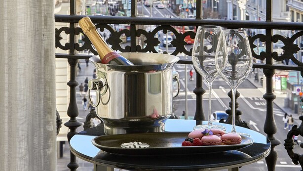 Un balcón con una mesa que sostiene una botella de champán, una tetera de plata y un plato con macarons y bayas.