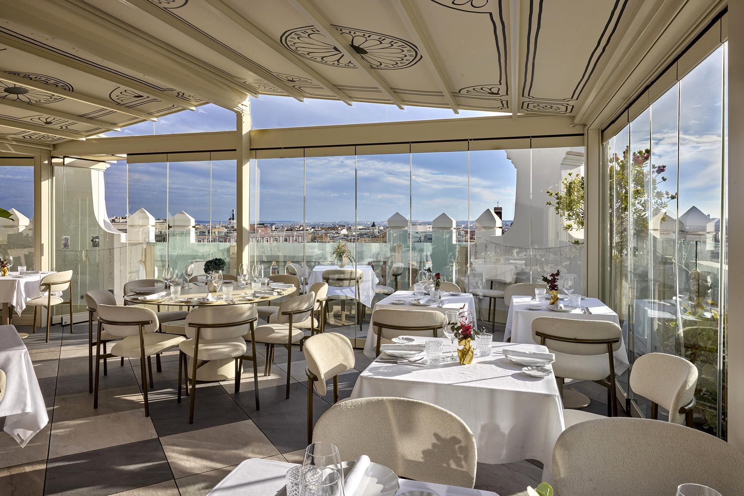 Un ristorante sul tetto con tavoli apparecchiati per mangiare, ampie finestre con vista sulla città e un soffitto decorativo.