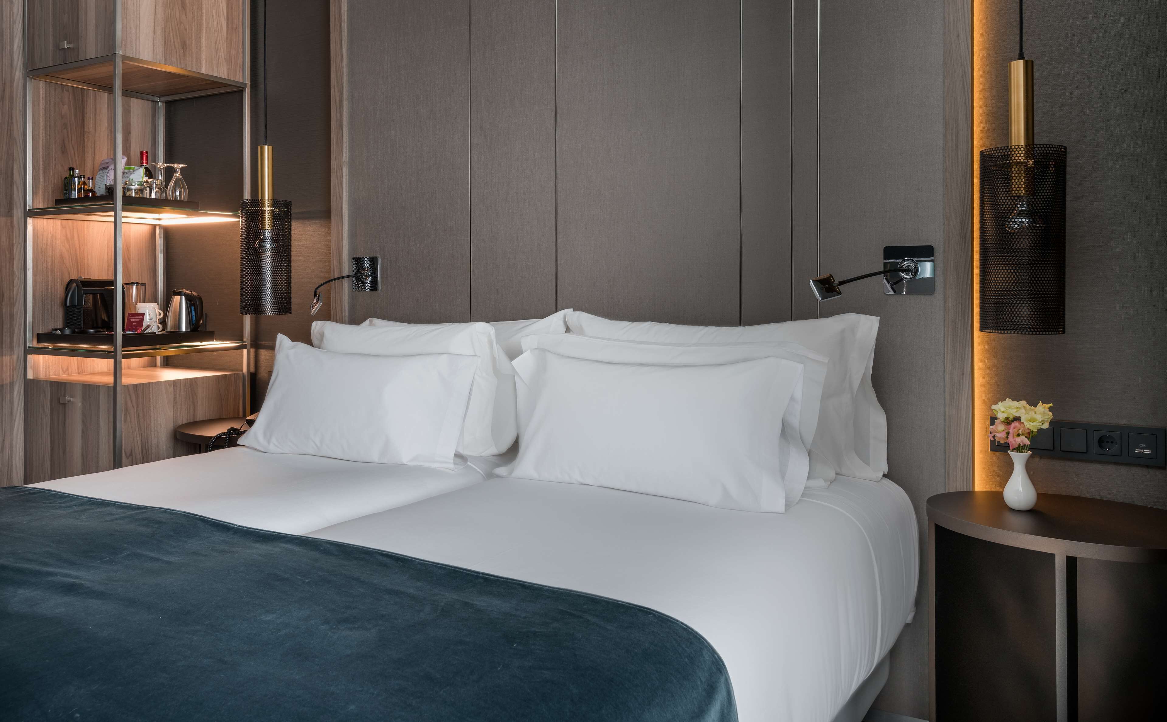 Una habitación de hotel moderna con una cama grande, una mesita de noche, una lámpara y un estante con artículos de aseo.