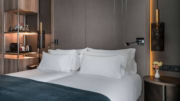 Una habitación de hotel moderna con una cama grande, una mesita de noche, una lámpara y un estante con artículos de aseo.