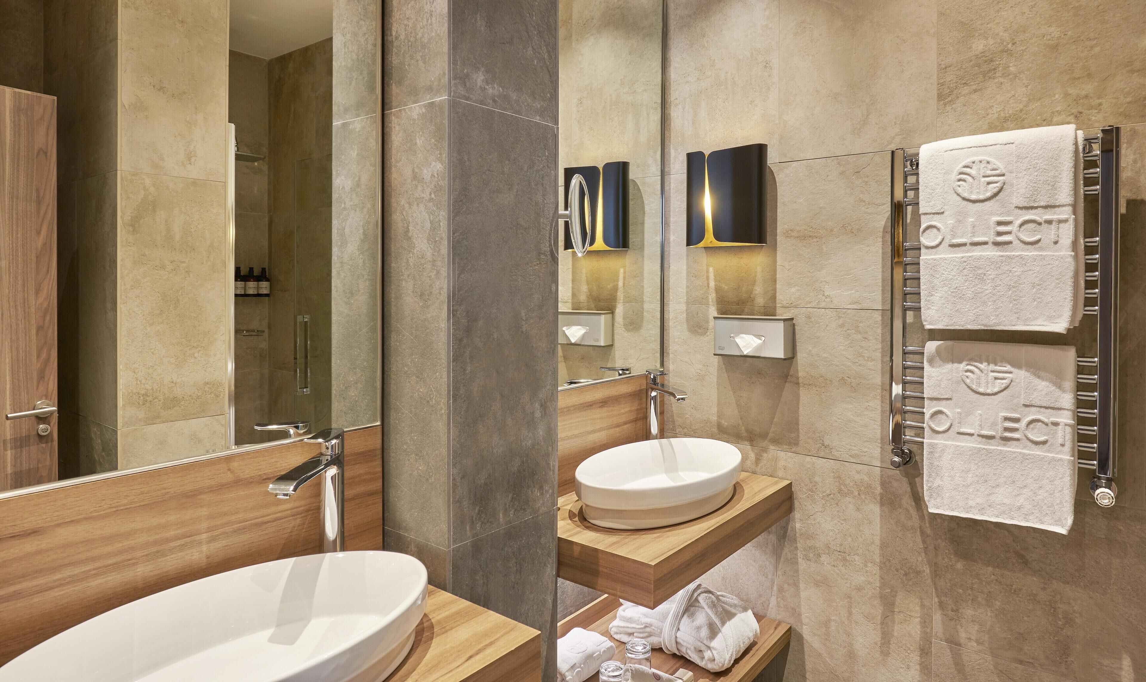 Un baño moderno con tocador de madera, un espejo grande, un toallero mural y un lavamanos empotrado.
