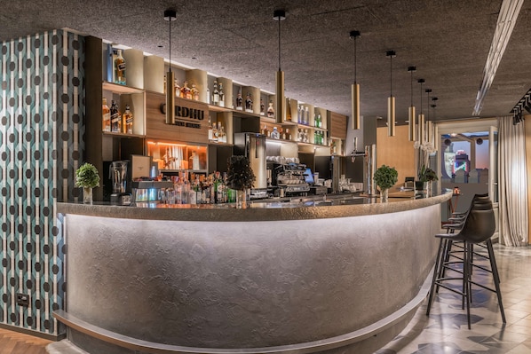 A modern bar area with a curved counter, shelves with bottles, and hanging pendant lights. - NH Collection Madrid Gran Vía (Madrid)