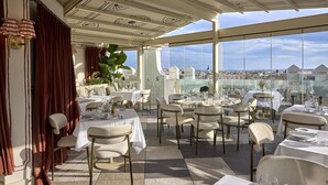 Un restaurante en la azotea con mesas listas para comer, amplios ventanales que ofrecen vistas de la ciudad y un techo decorativo.