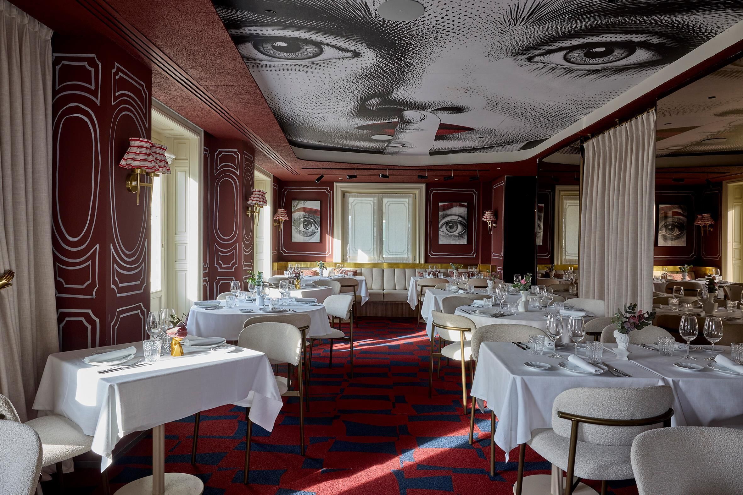 A restaurant with tables set for dining, a patterned carpet, and a ceiling mural.