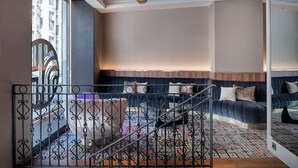 Una habitación de hotel moderna con una cama grande, una zona de estar con un sofá y sillones, y una escalera con barandilla decorativa.