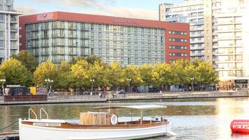 Un hotel con fachada de vidrio moderna, vistas al agua y un barco fondeado cerca.