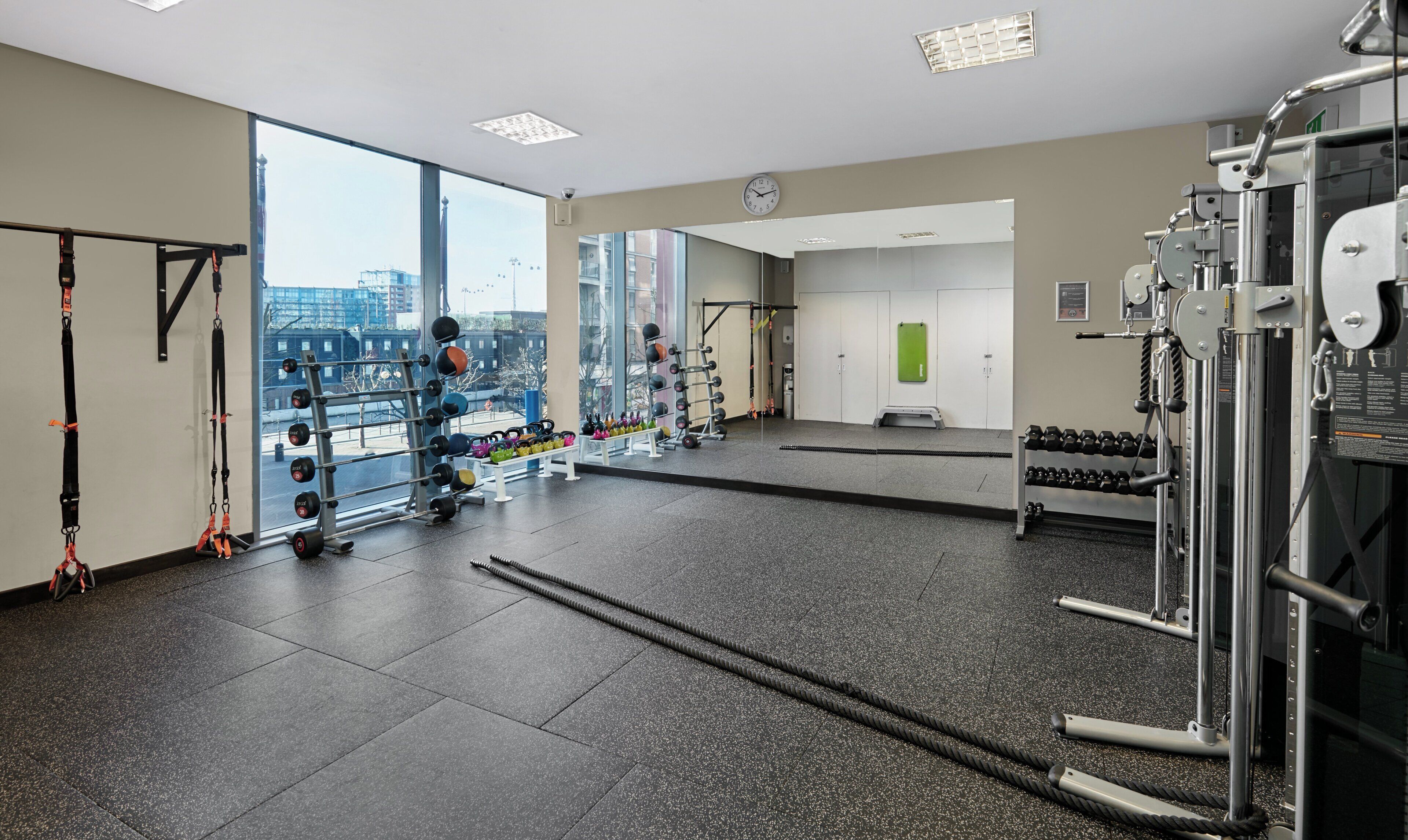 A gym with various exercise equipment, large windows, and a view of the city.