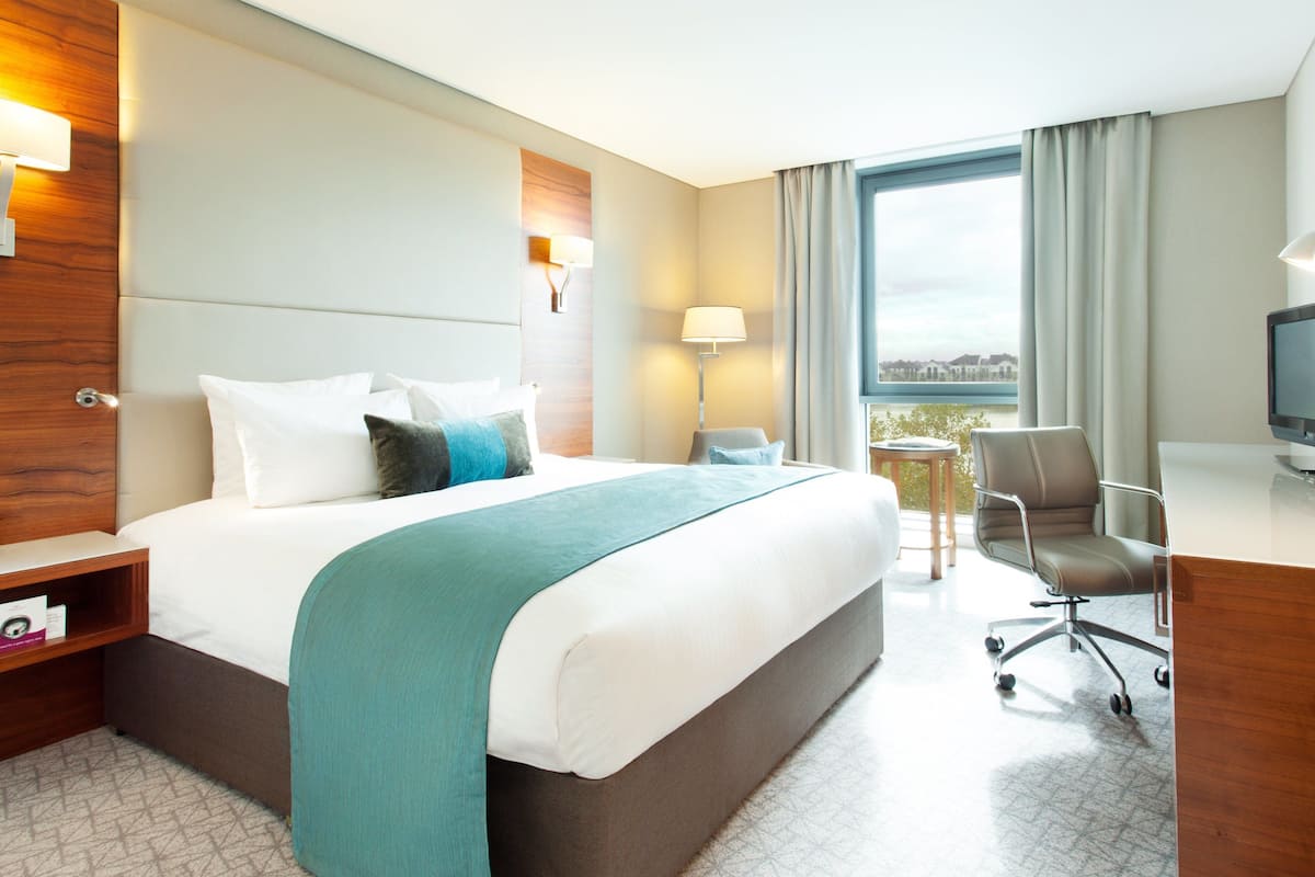 Een hotelkamer met een groot bed, een bureau met telefoon, een stoel, een televisie en een raam met uitzicht.