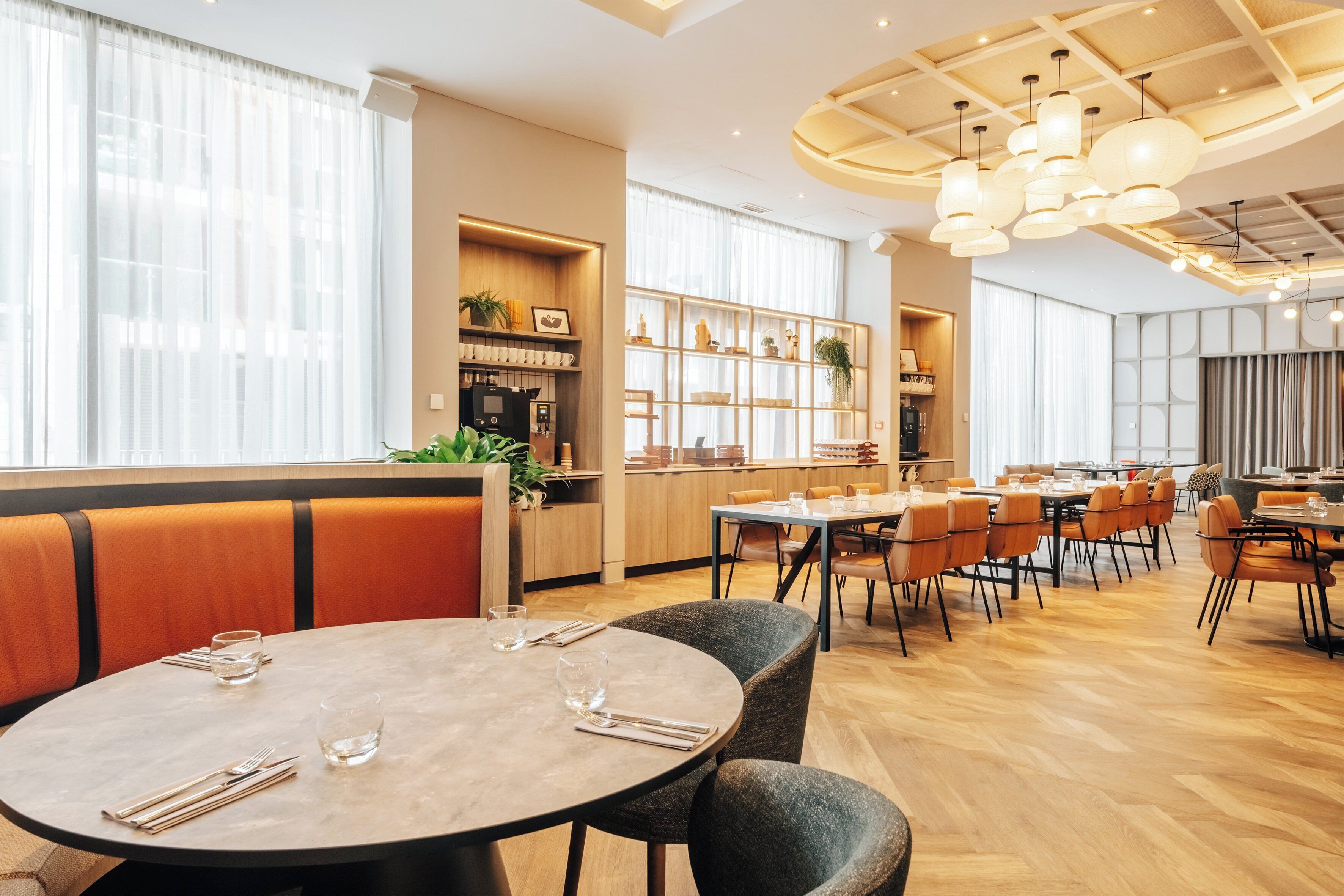 A modern restaurant with round tables, orange booths, and wooden flooring.