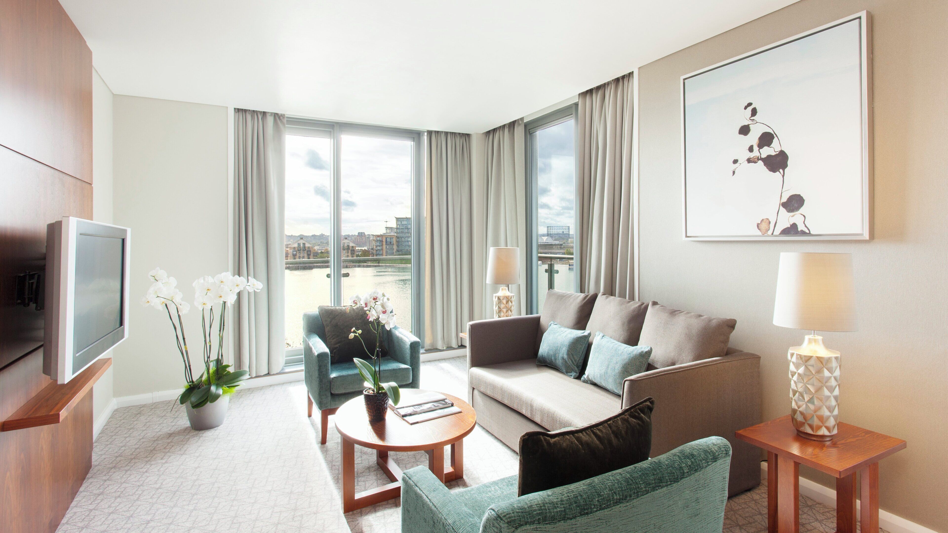Una habitación de hotel moderna con sofá, sillones, una mesa de centro, televisor y un ventanal con vistas a la ciudad.