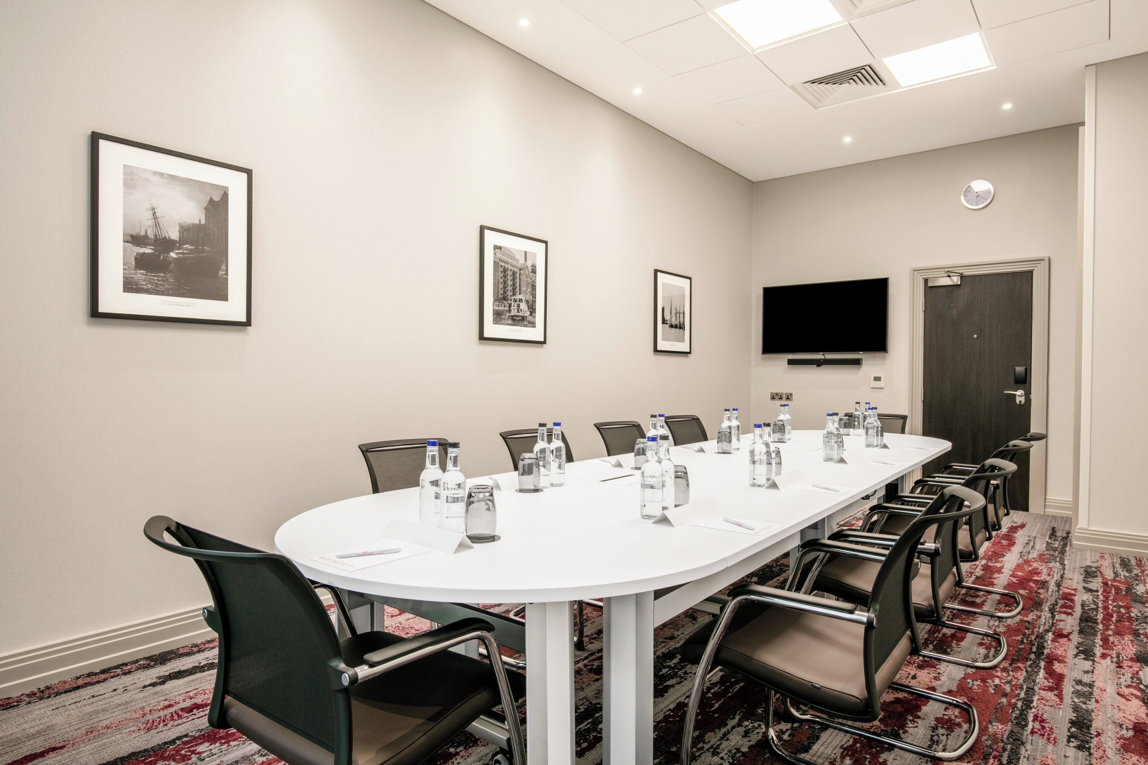 A conference room with a long table, chairs, water bottles, and framed pictures on the walls.