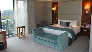 A hotel room with a large bed, a small side table, a sofa, a window with curtains, and a city view. - Crowne Plaza London - Docklands by IHG (London)