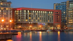 A modern hotel with a red facade, large windows, and a view of the water. - Crowne Plaza London - Docklands by IHG (London)