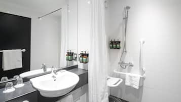 Un baño moderno con un lavamanos grande, un espejo, una ducha y artículos de tocador en la pared.