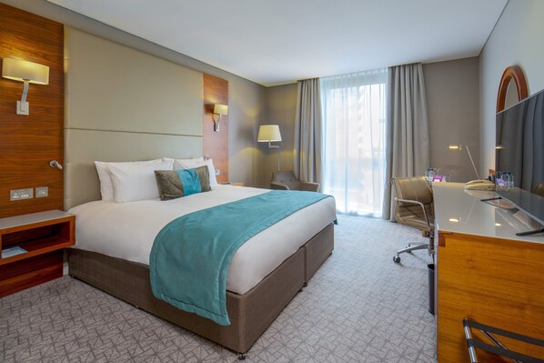 A hotel room with a large bed, a desk, a chair, a desk lamp, and a mirror.