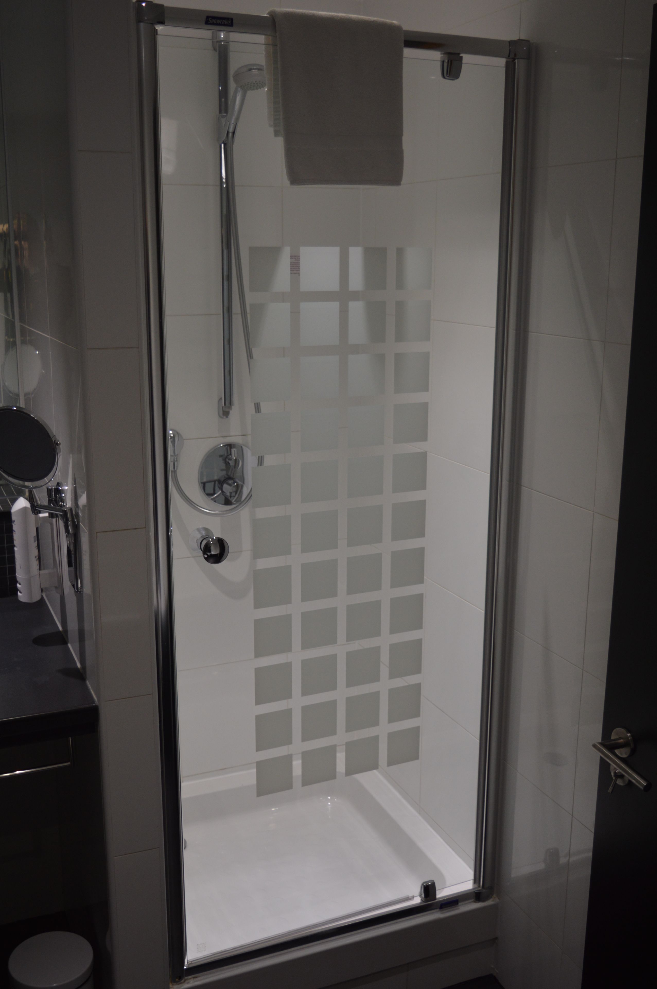 Eine gläserne Dusche mit weiß gefliesten Wänden, einer sichtbaren Duschbrause und einem Handtuch an der Tür.