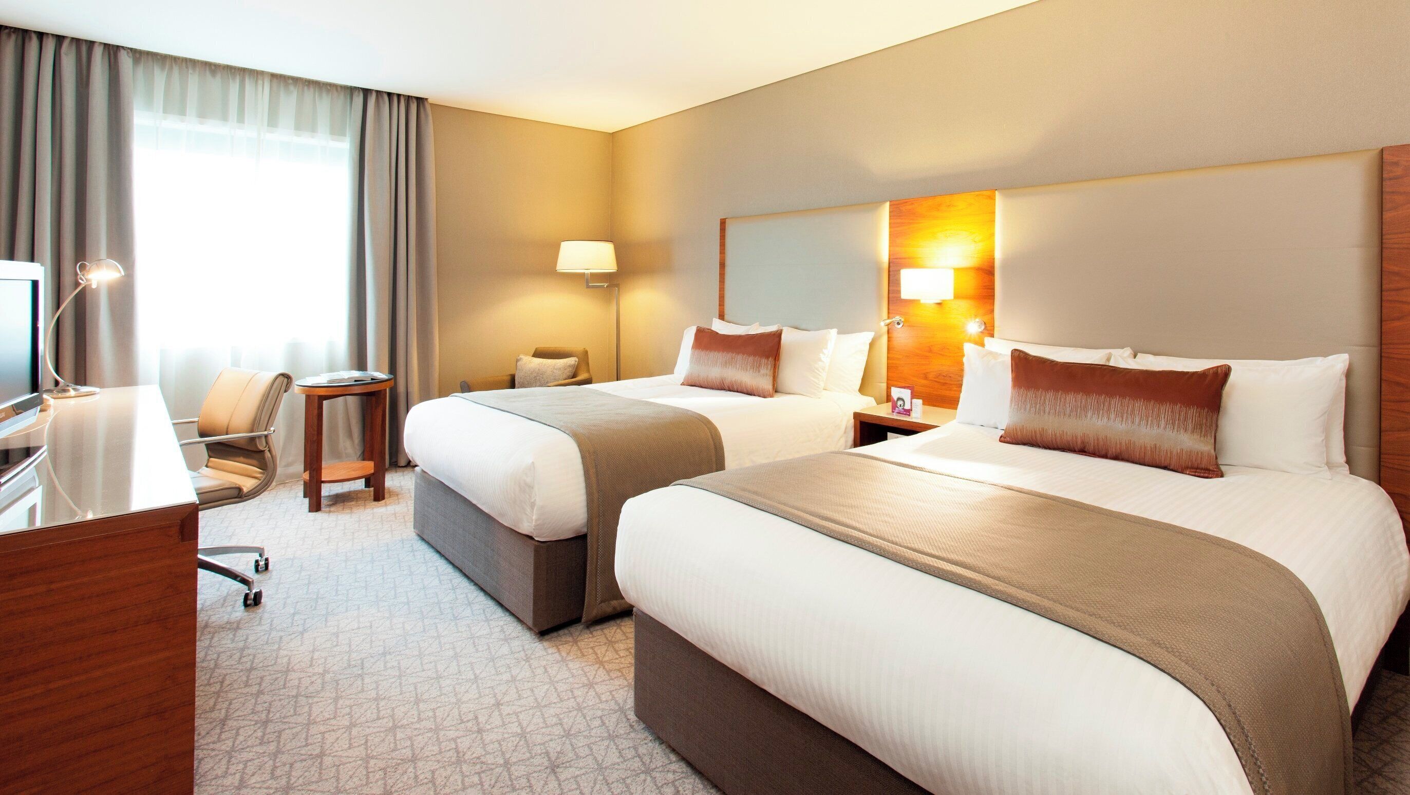 Een hotelkamer met twee bedden, een bureau, een stoel, een lamp en een nachtkastje.