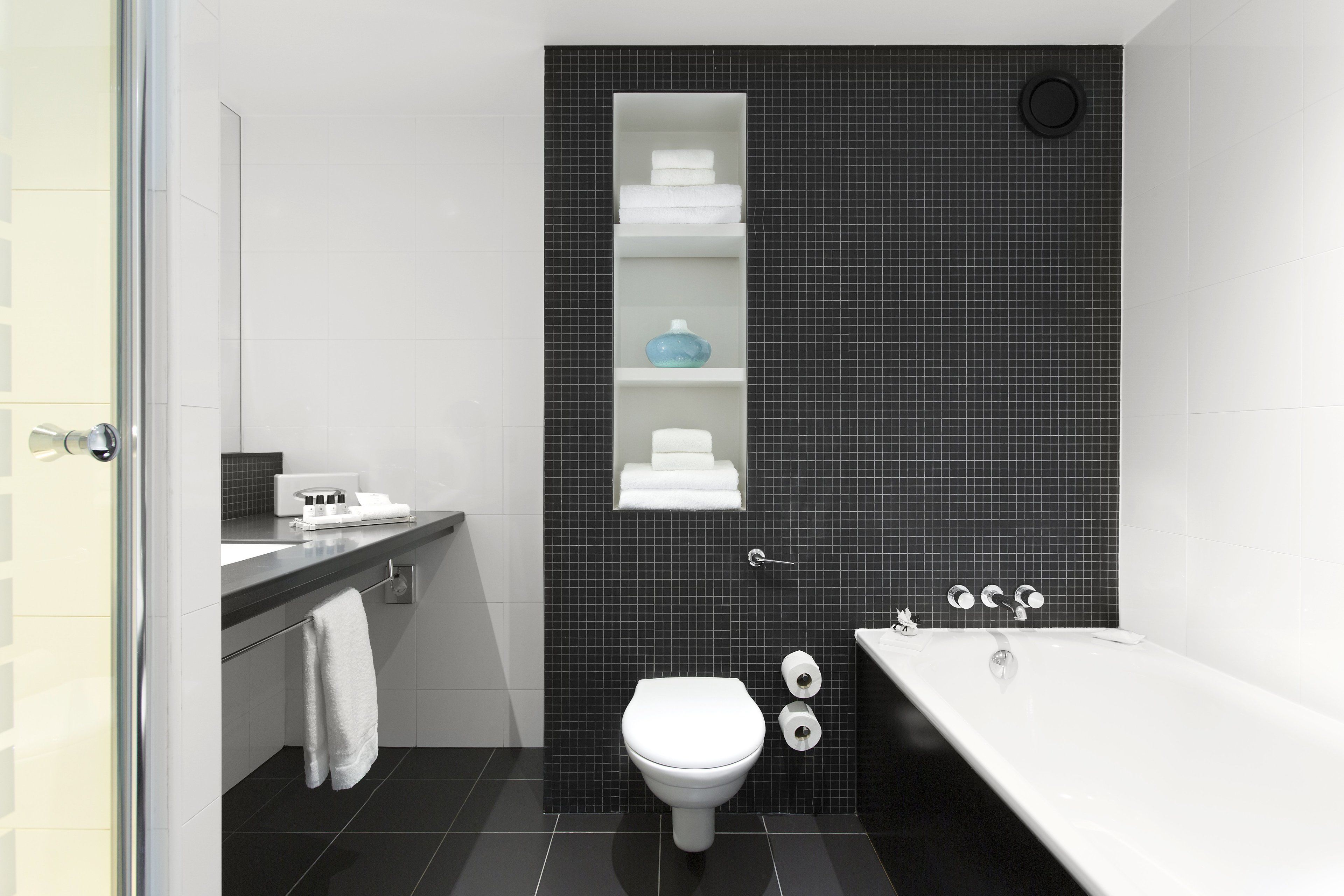 A modern bathroom with a white toilet, a bathtub, and a shelf with toiletries.