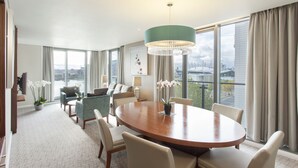 A spacious hotel room with a large round table, comfortable seating, a chandelier, and a view of the city through large windows. - Crowne Plaza London - Docklands by IHG (London)