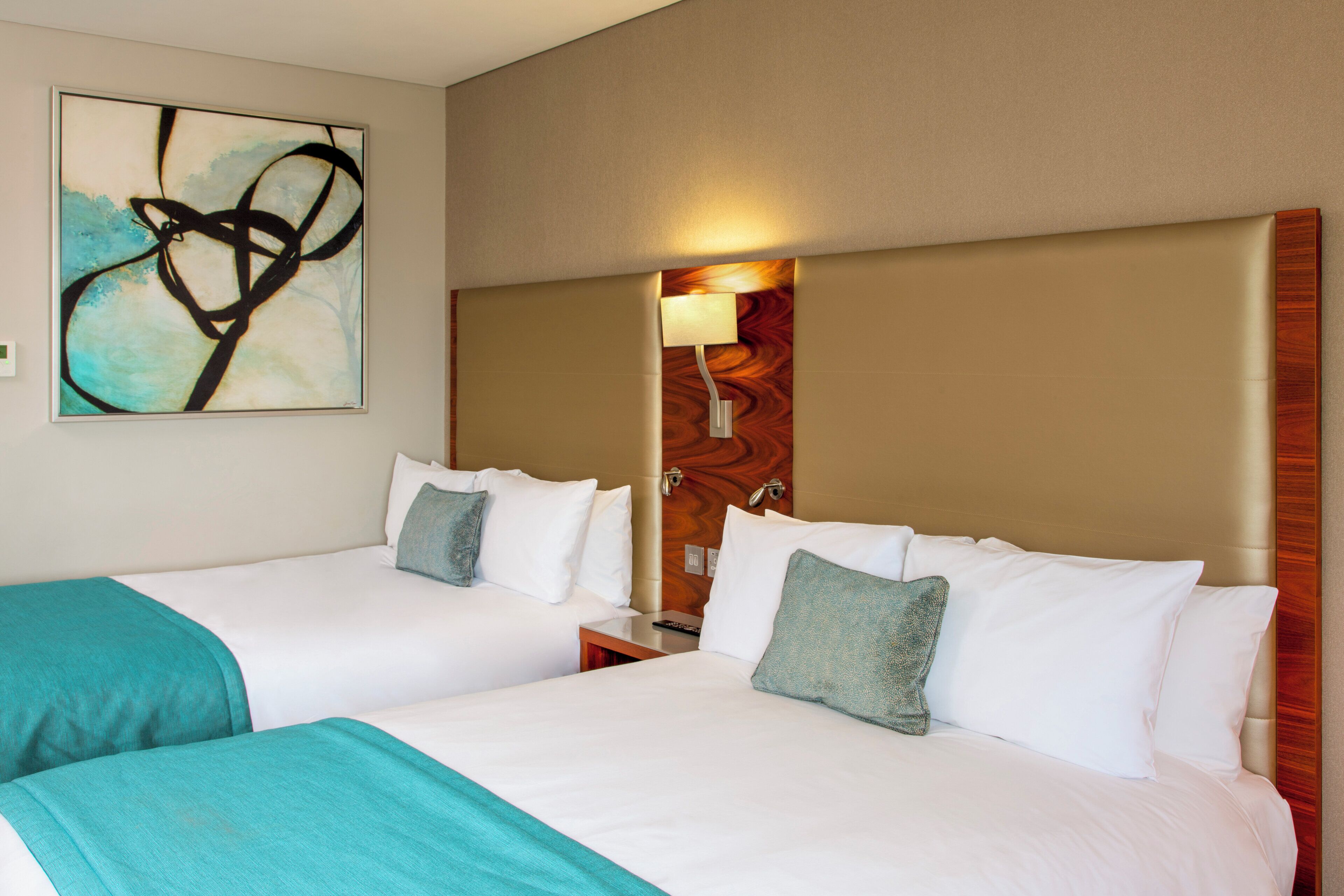 A hotel room with two beds, a wooden headboard, a wall-mounted artwork, and a bedside lamp.