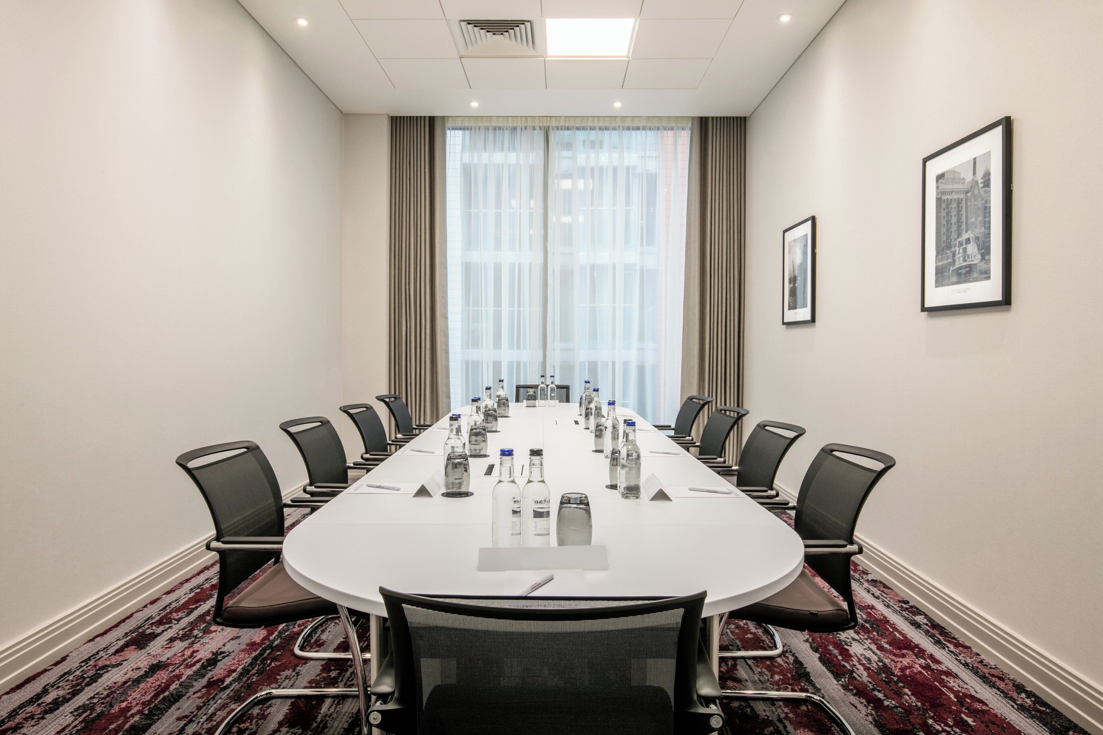 A conference room with a long table, chairs, water bottles, and framed pictures on the walls.