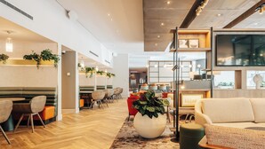 A modern hotel lobby with wooden flooring, seating areas, and a large potted plant. - Crowne Plaza London - Docklands by IHG (London)