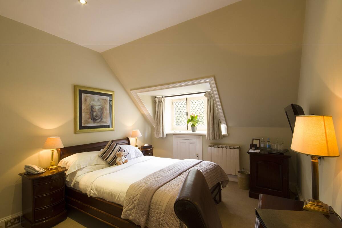 A bedroom with a bed, bedside tables, a lamp, a window with curtains, a radiator, and a plant.