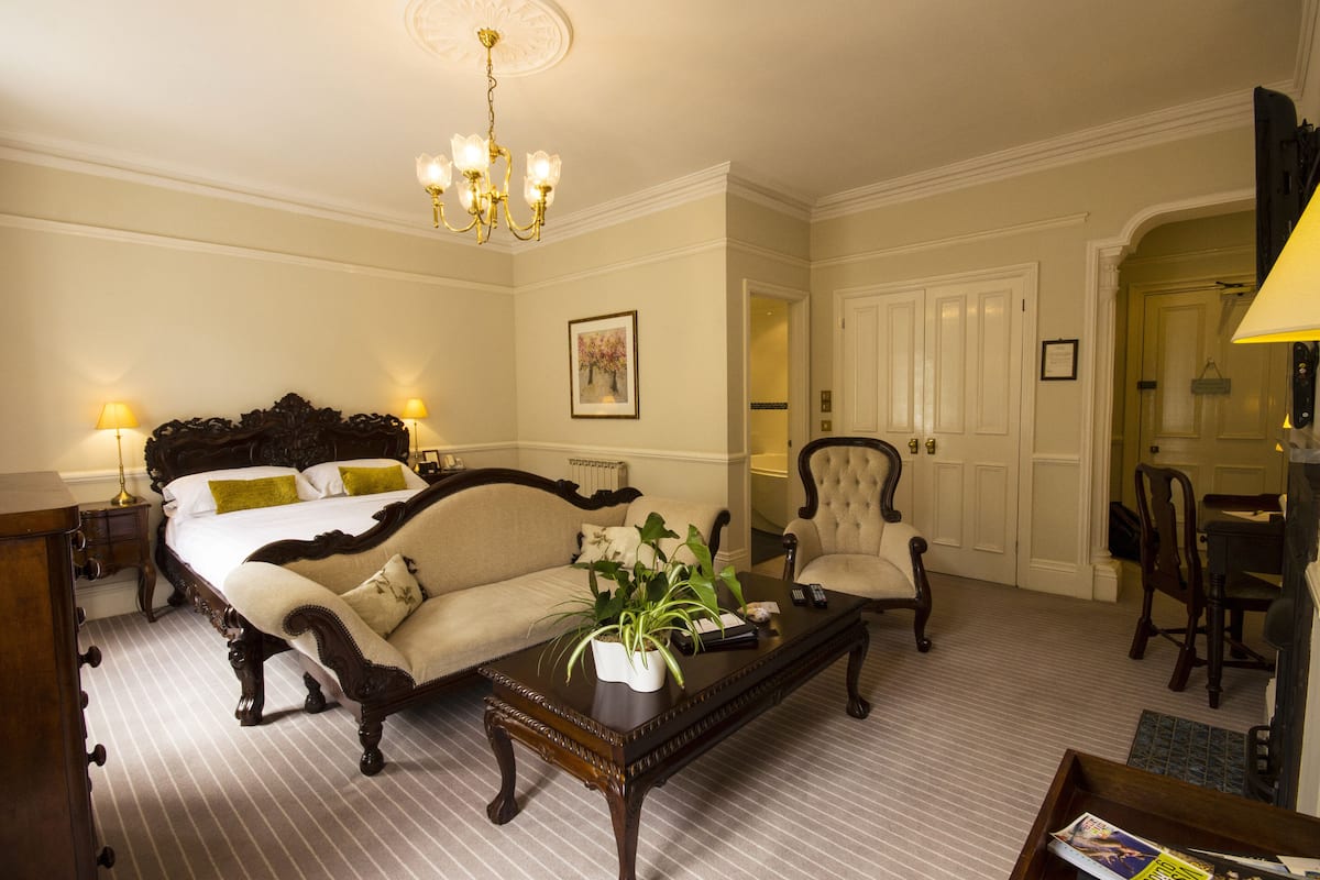 A hotel room with a large bed, a sitting area with a sofa and armchairs, a coffee table with a plant, and a chandelier.