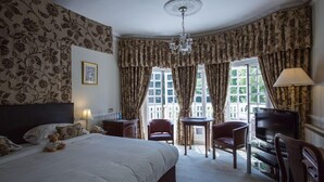 Una habitación de hotel con una cama grande, un escritorio, una silla, un televisor y una ventana con cortinas.