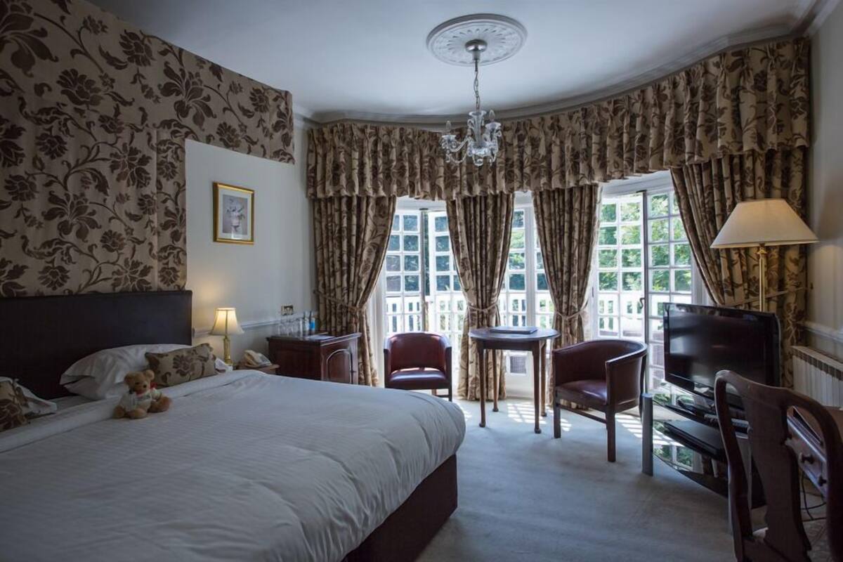 A hotel room with a large bed, a desk, a chair, a television, and a window with curtains.