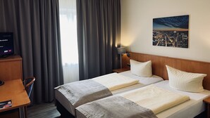 Een hotelkamer met twee bedden, een bureau, een televisie en een stadslandschap op de muur.
