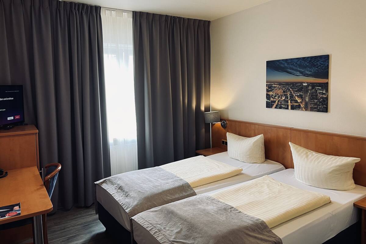 Una habitación de hotel con dos camas, un escritorio, un televisor y un cuadro de la ciudad en la pared.
