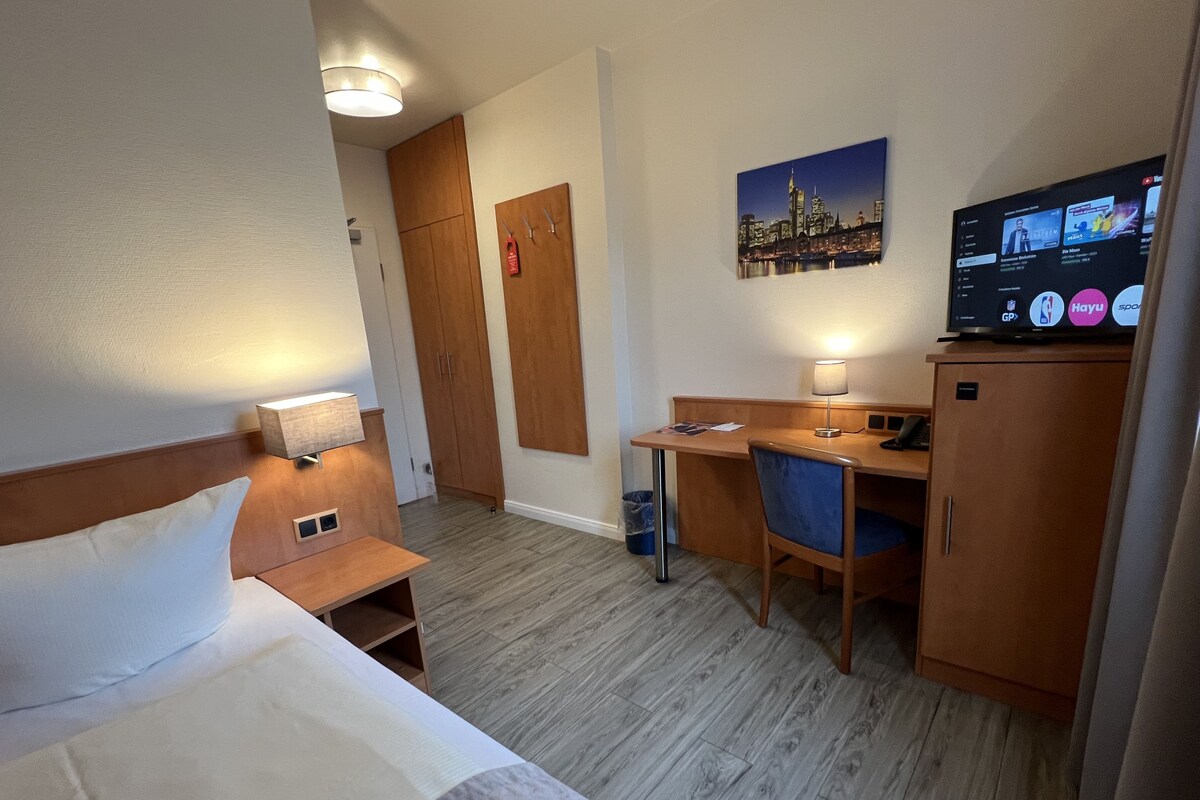 Habitación de hotel con cama, escritorio, silla y televisor mostrando un canal deportivo.