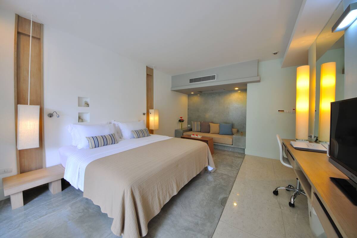 Ein Hotelzimmer mit Bett, Nachttischen, Schreibtisch mit Stuhl, Fernseher und Wandleuchten.