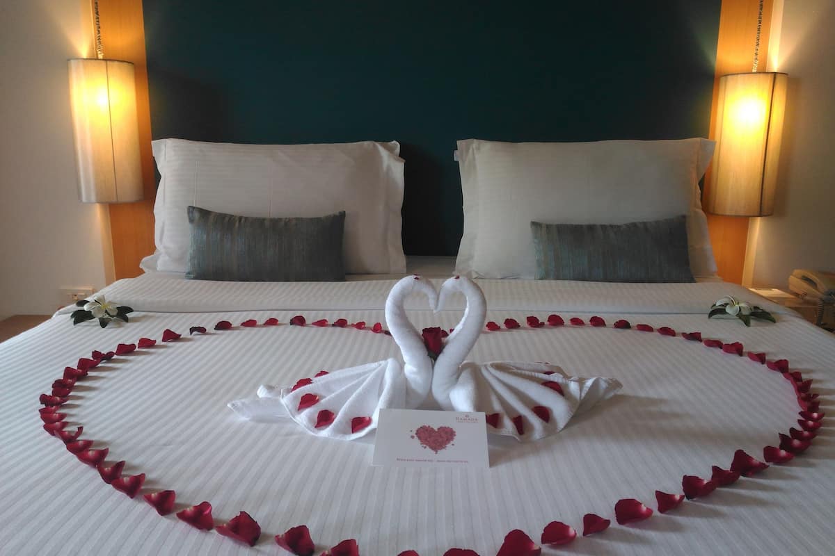 Ein Hotelzimmer mit einem Bett, dekoriert mit einer herzenförmigen Anordnung aus Rosenblättern und Handtüchern.