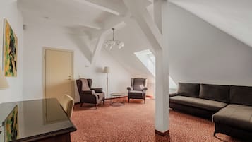 A spacious loft with a high ceiling, a large window, a brown sofa, two armchairs, a small round table, and a desk with a chair.
