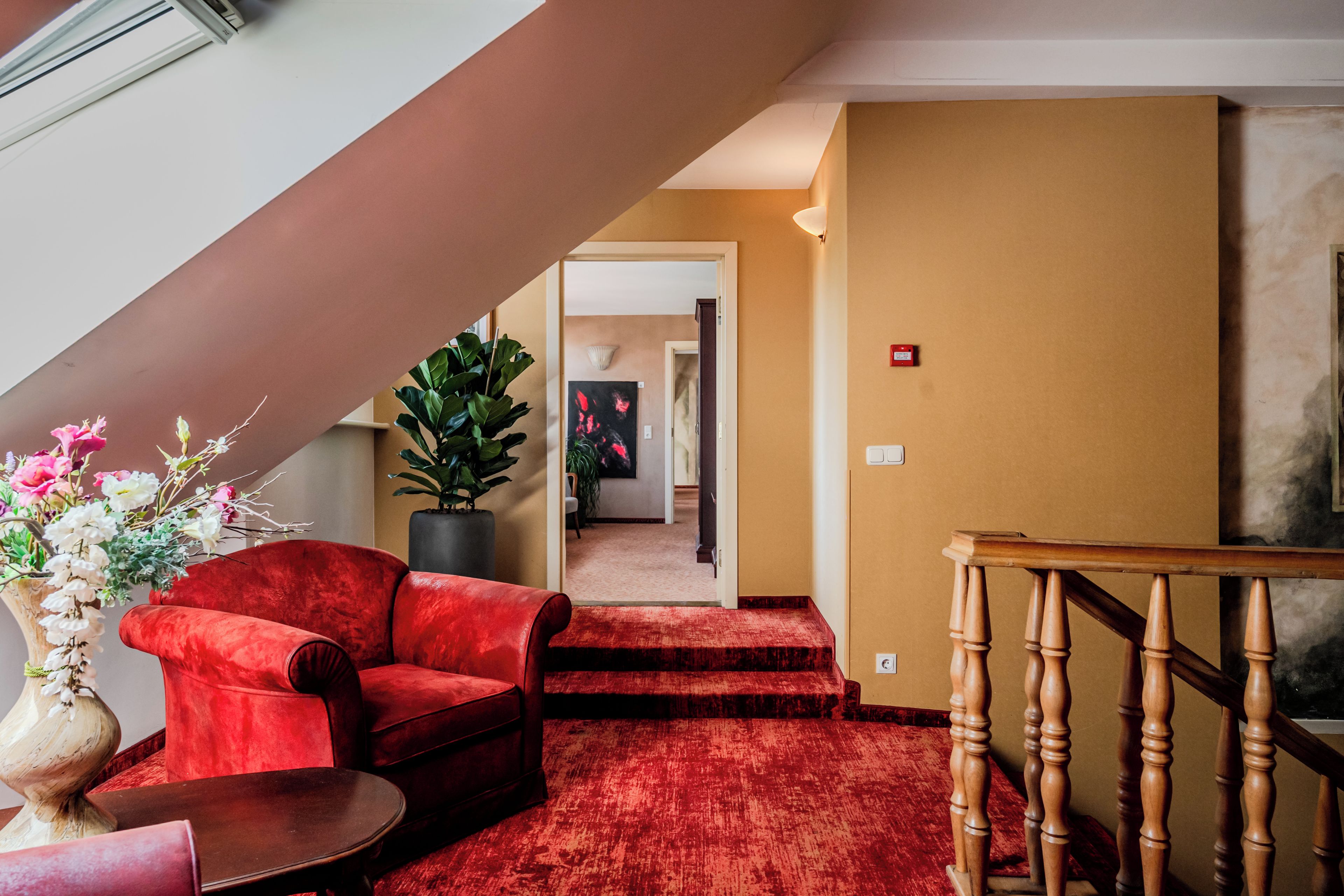 Un sofá de terciopelo rojo, una escalera de madera y un suelo cubierto de alfombra roja en el vestíbulo de un hotel.
