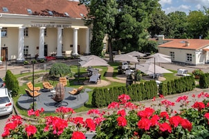 Un hotel con un patio que cuenta con asientos al aire libre, una piscina y un jardín con flores rojas.