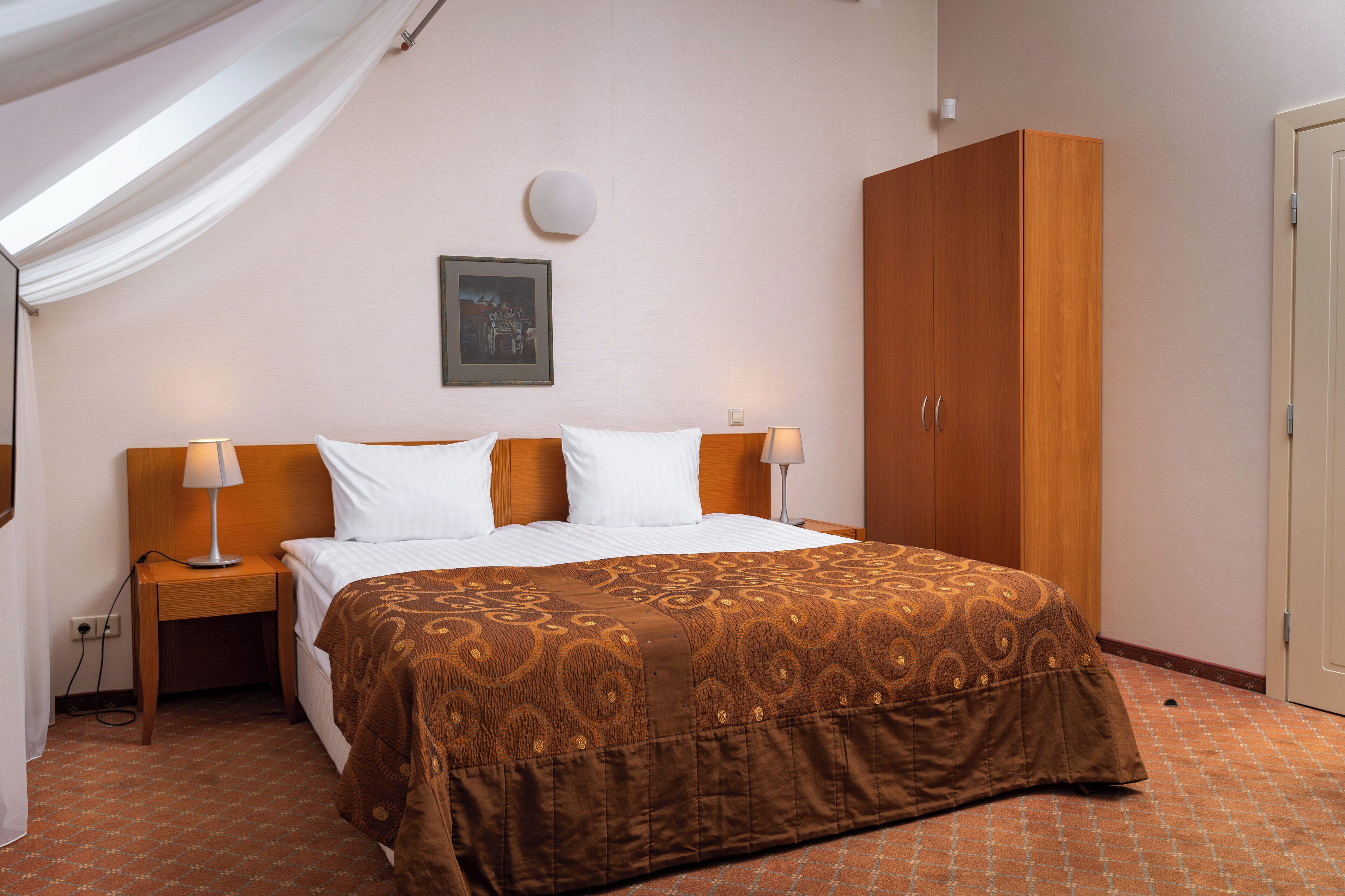 Una camera d'albergo con un letto grande, una testiera in legno, due comodini con lampade, un armadio e un quadro appeso al muro.