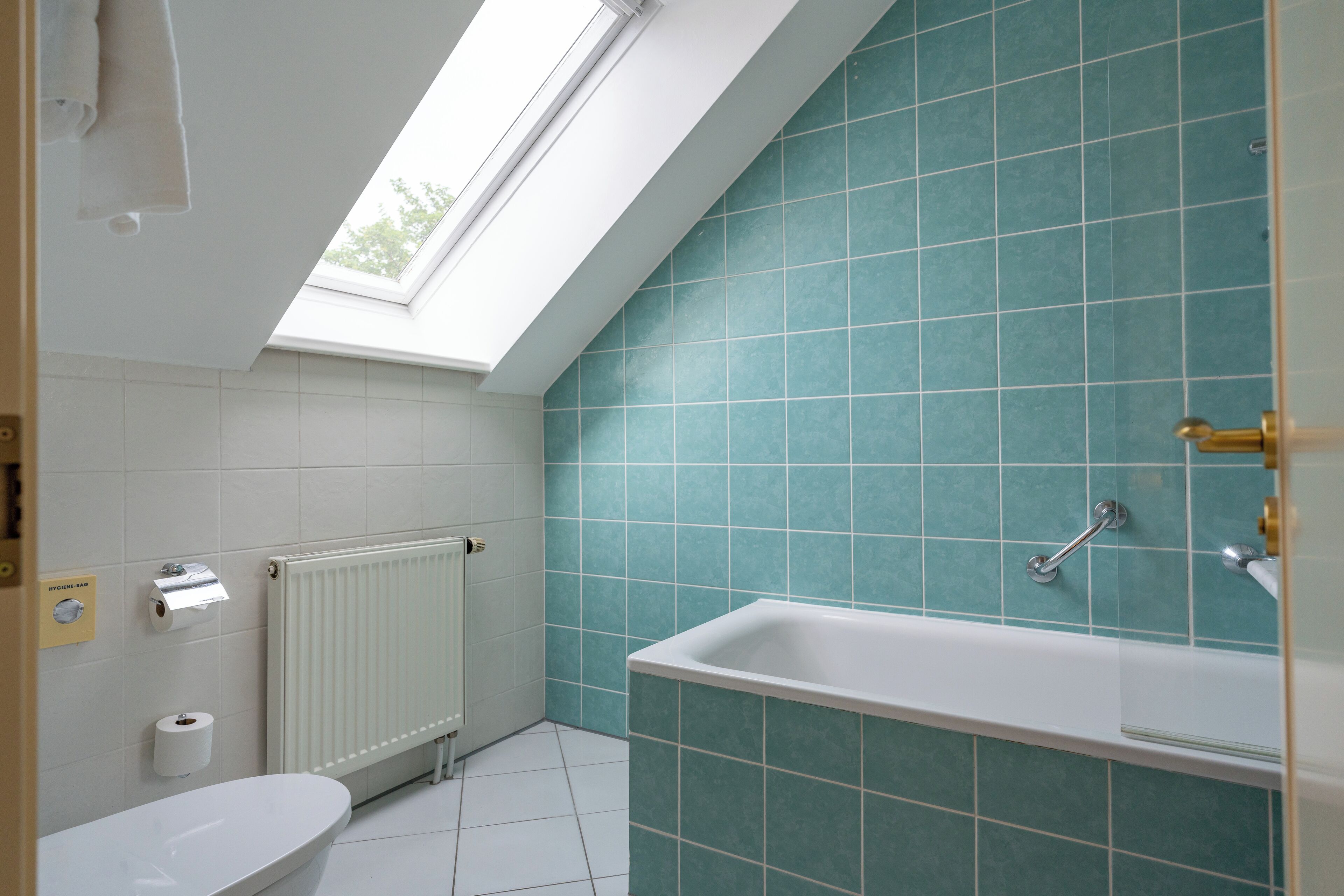 A bathroom with a skylight, a bathtub, a toilet, and a radiator.