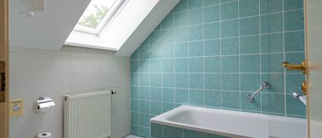 A bathroom with a skylight, a bathtub, a toilet, and a radiator.