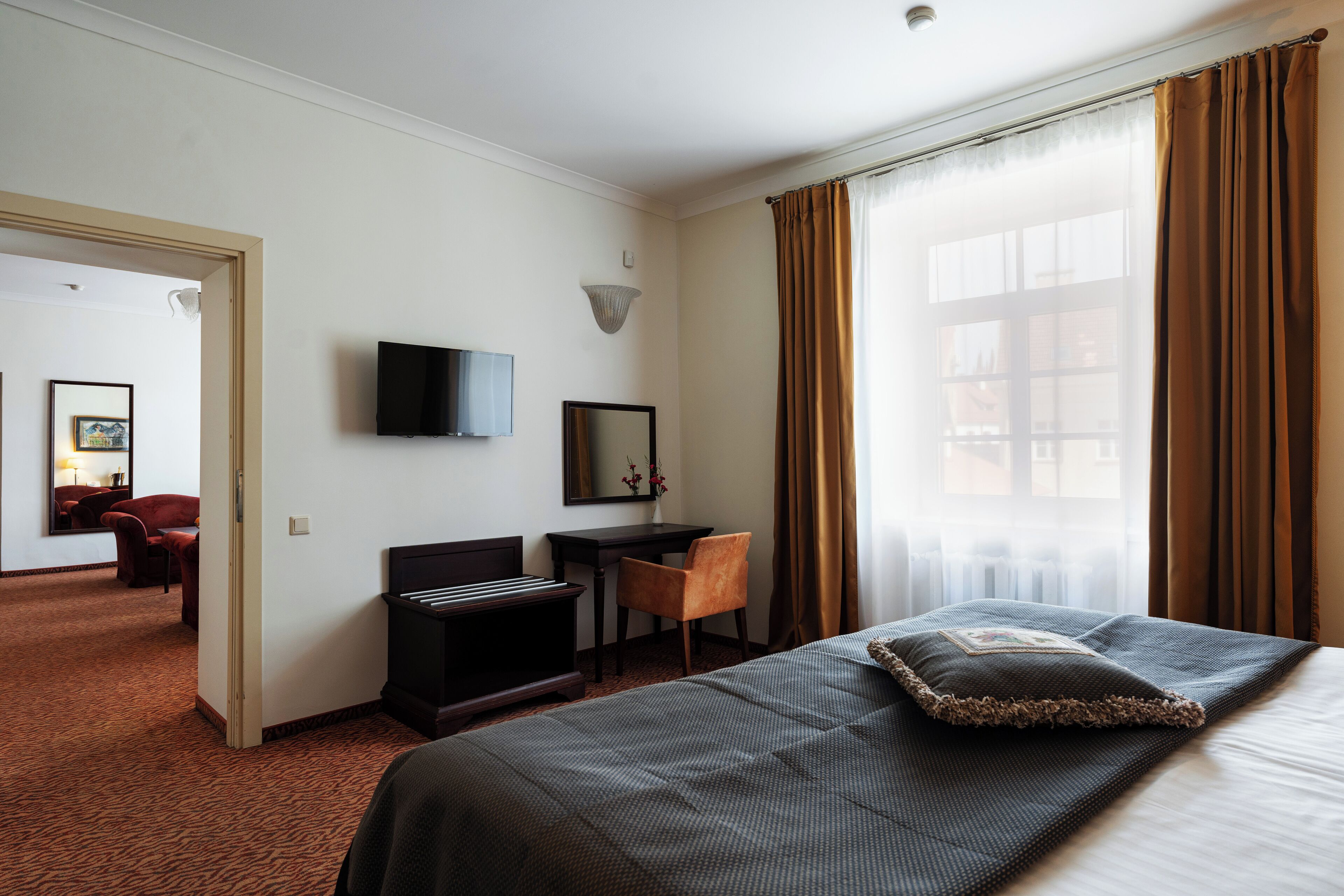 A hotel room with a bed, a desk, a chair, a TV, and a window with curtains.