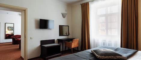 A hotel room with a bed, a desk, a chair, a TV, and a window with curtains.