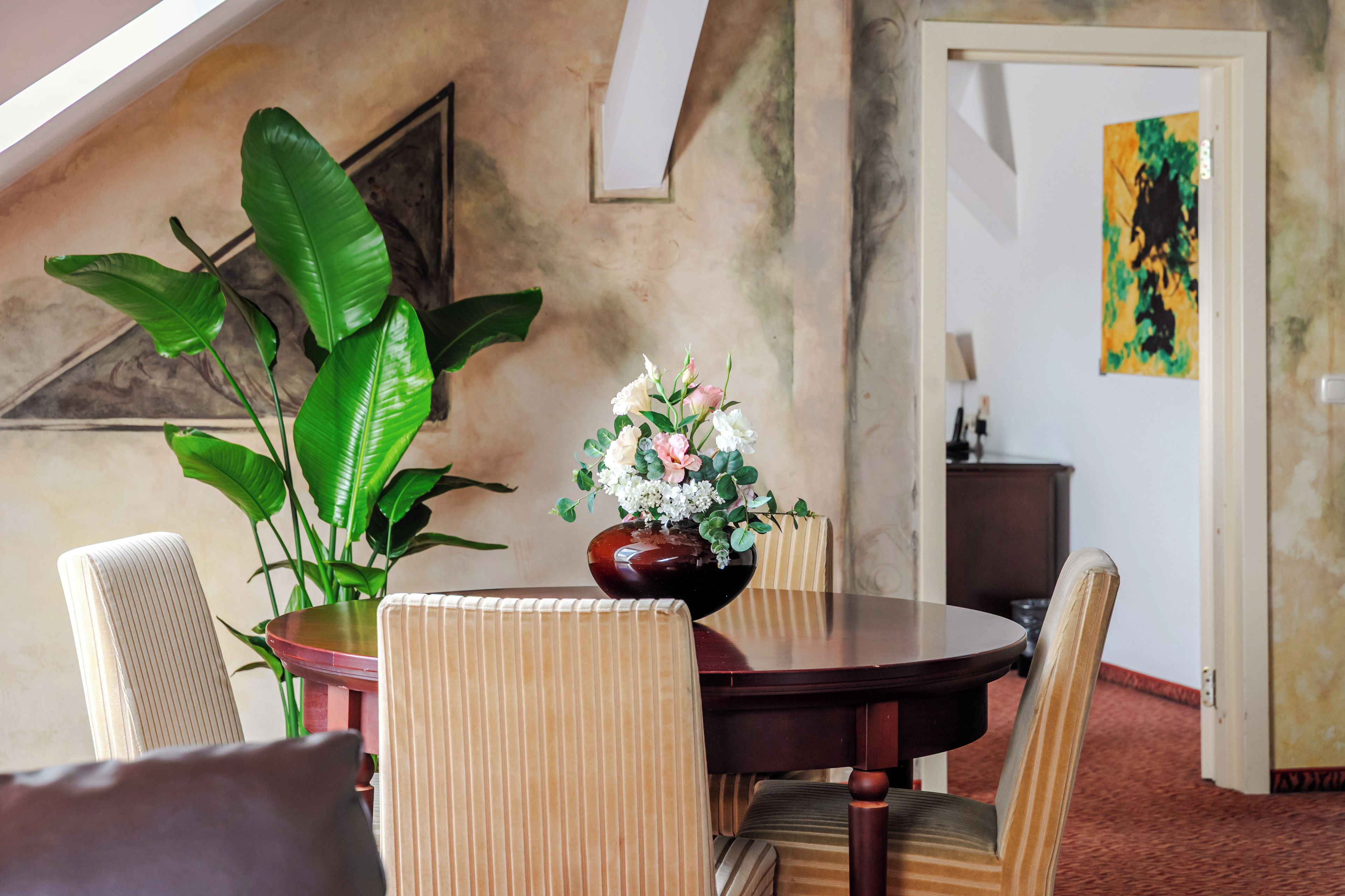 A dining area with a round table, chairs, a vase of flowers, and a large plant.