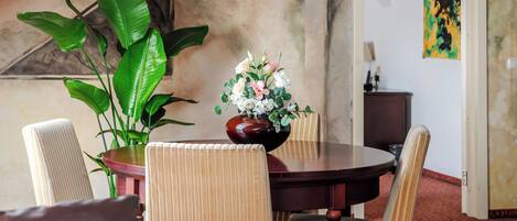 A dining area with a round table, chairs, a vase of flowers, and a large plant.
