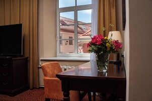Habitación de hotel con televisor, escritorio con un florero, una silla y ventana con vistas a edificios.