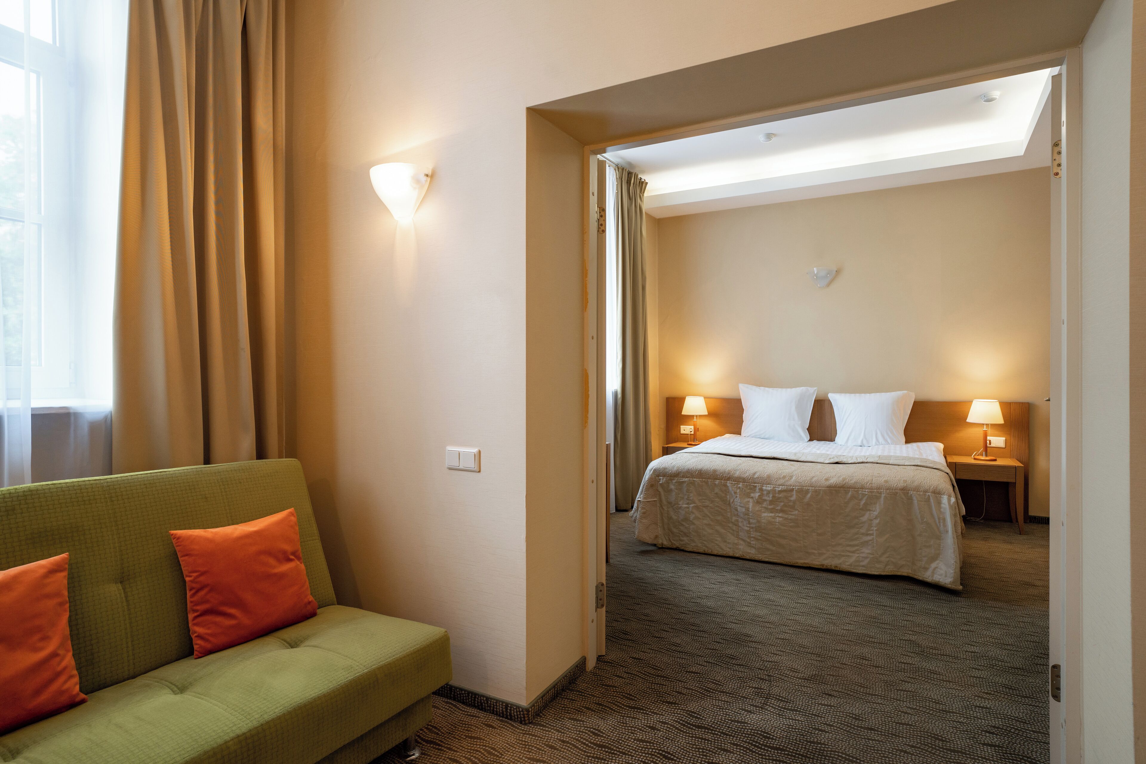Una habitación de hotel con un sofá verde, una cama con ropa blanca y dos lámparas de noche.